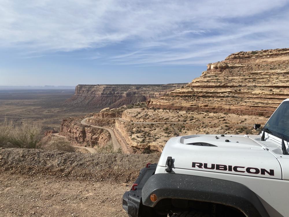 View from a Jeep's hood of the switchbacking Moki Dugway road descending through layered sandstone cliffs near Mexican Hat.