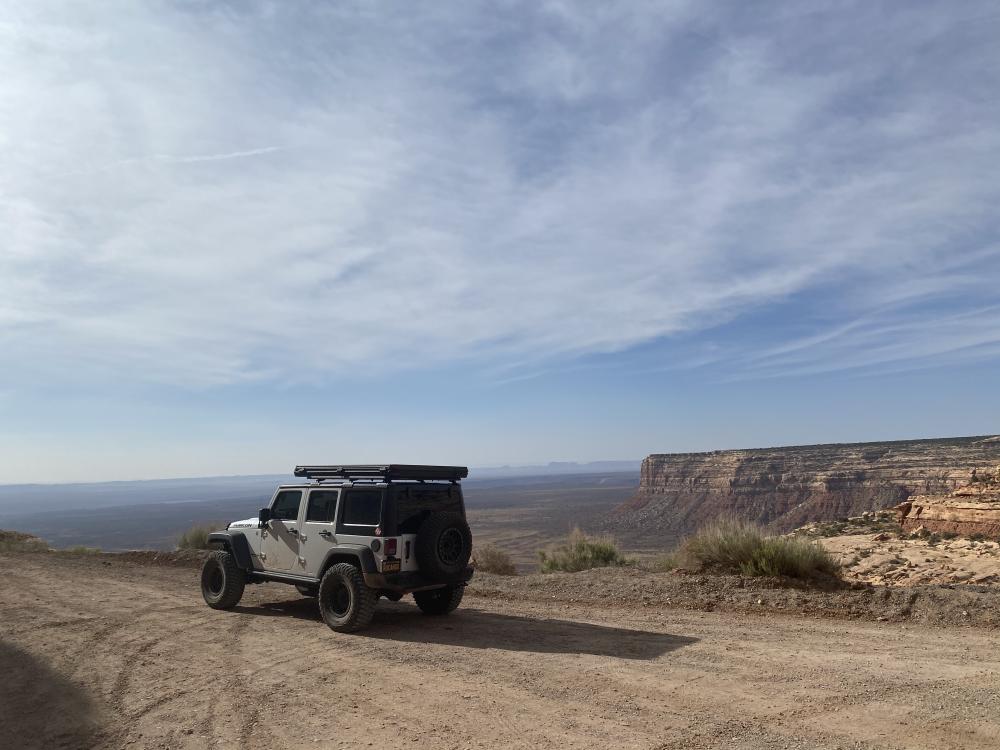 White Jeep Wrangler parked on a dirt overlook above the sweeping desert plateau near Mexican Hat, Utah.