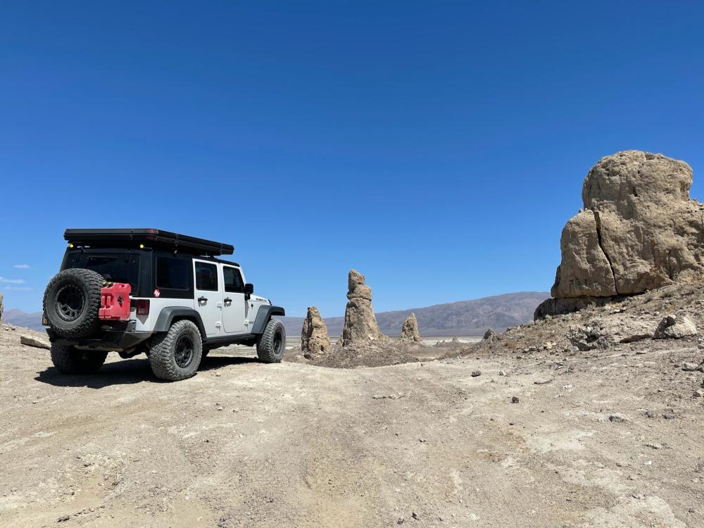 White Jeep Wrangler parked near rock spires at Trona Pinnacles, with desert mountains stretching to the horizon.
