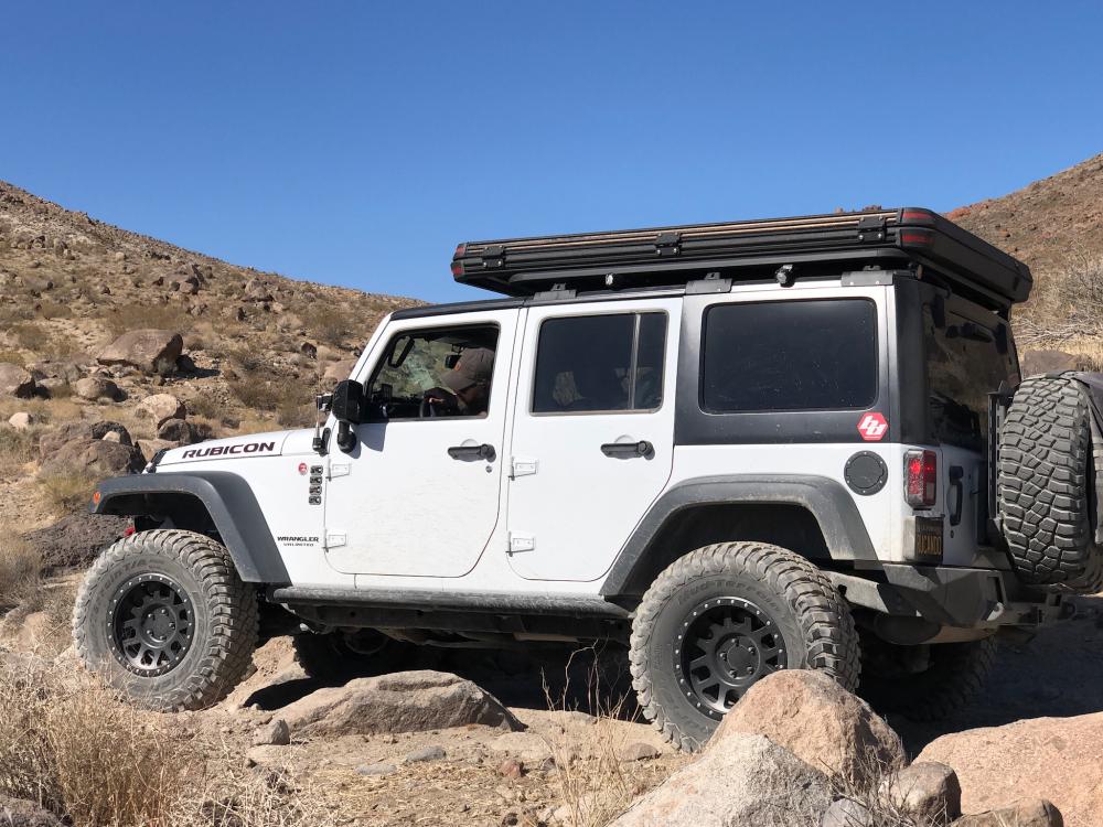 White Jeep Wrangler Rubicon crawling over a boulder field on a rocky desert trail.