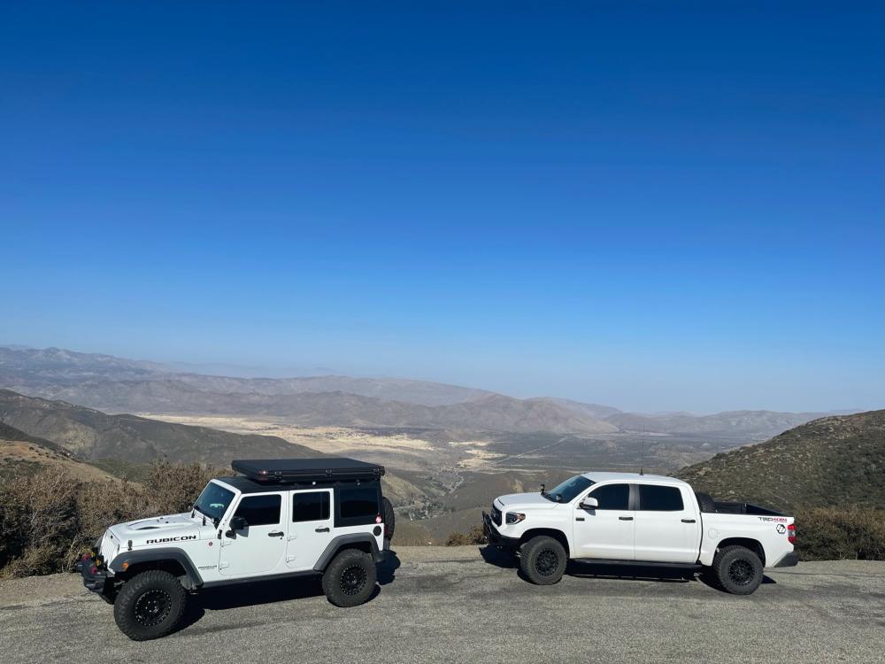 White Toyota Tundra and Jeep Wrangler parked at a scenic overlook above Anza-Borrego's badlands, with mountains and desert stretching to the horizon.
