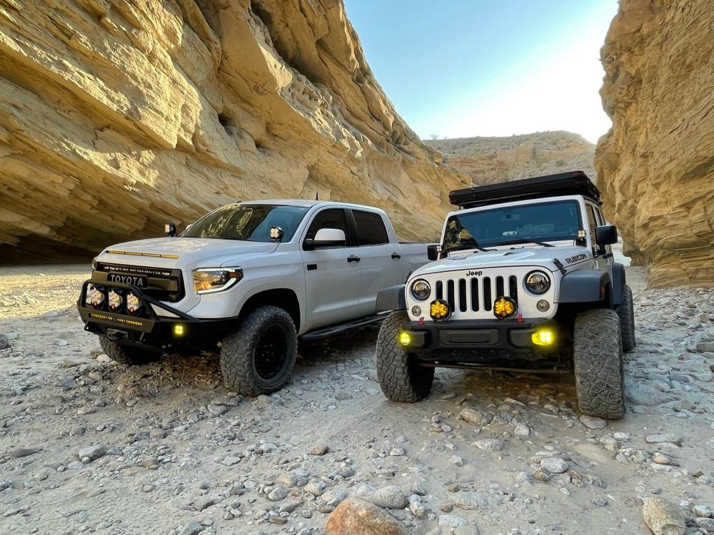 White Toyota Tundra and Jeep Wrangler parked side by side inside a narrow sandstone slot canyon.
