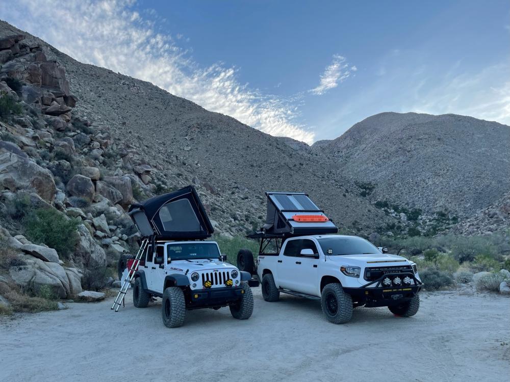Jeep Wrangler and Toyota Tundra with rooftop tents popped up at a rocky desert campsite in the evening light.